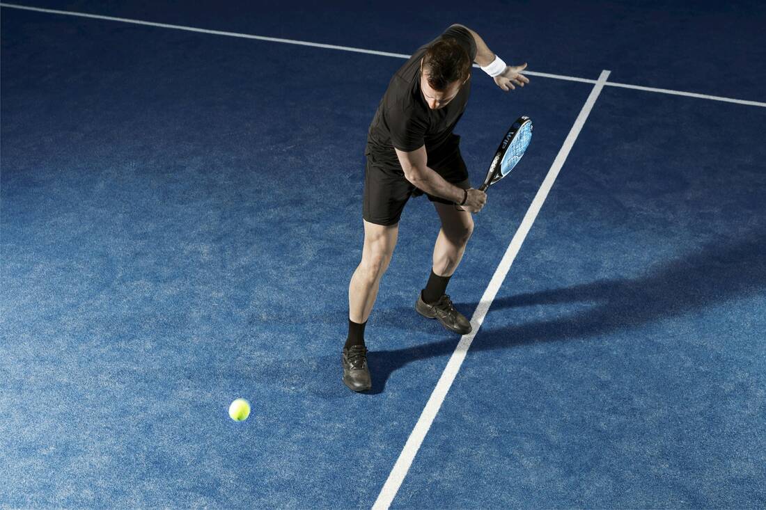 Padel player hitting a backhand during a game on a blue court