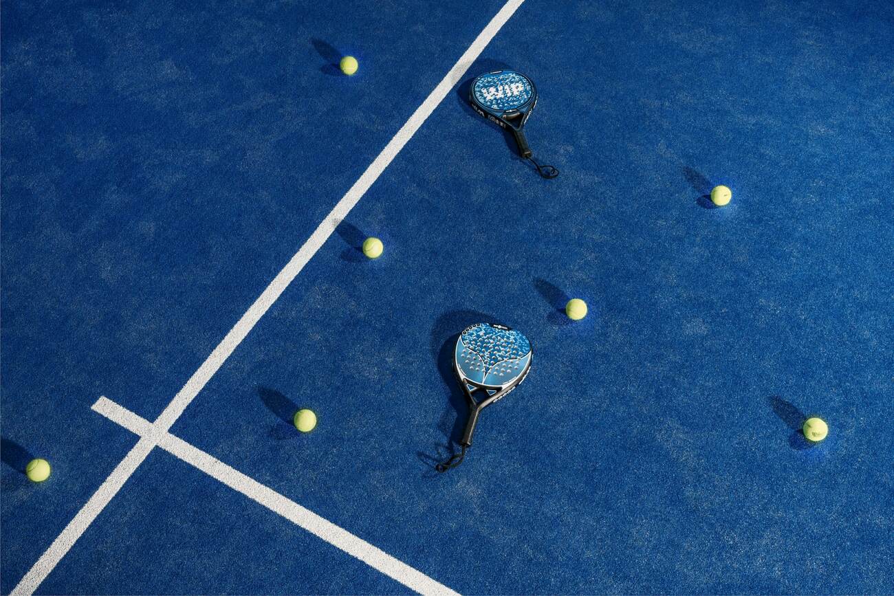 Padel paddles and balls scattered on a blue padel court, seen from above